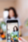 A mobile phone taking a photo of a woman preparing food, the mobile screen shows the shot with a blurred background of the shot