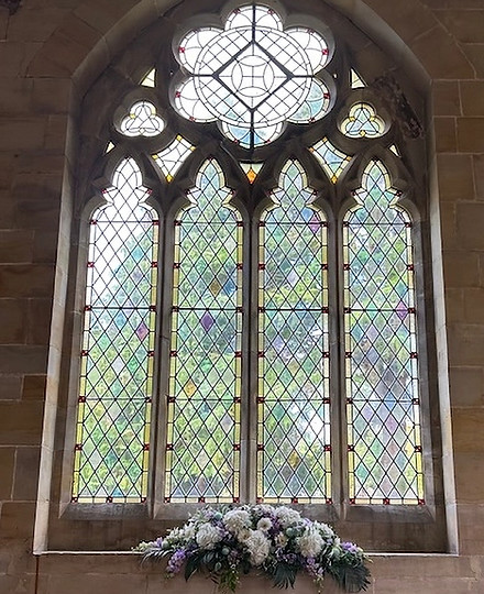 A beautiful stained glass arched window in a funeral chapel with an arrangement of flowers underneath