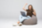 mulher-jovem-sentada-no-pufff-com-laptop-com-gesto-de-vitoria-isolado-na-parede-branca.jpg