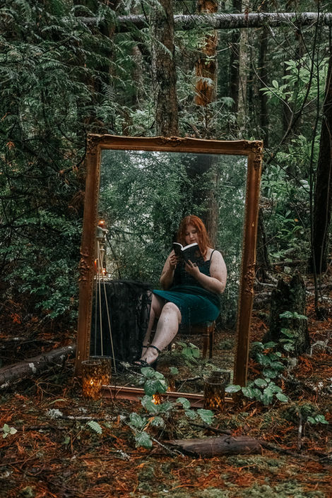 Woman reading in a mirror, in a forest, holding a book Evergreen Girls LLC