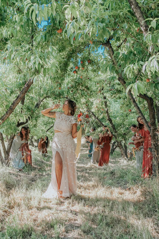 Woman in white dress stands under a tree. Friends and Weddings & Unions.