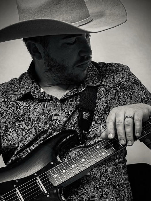 Martin Boyd looking down with guitar in a thoughtful studio portrait.