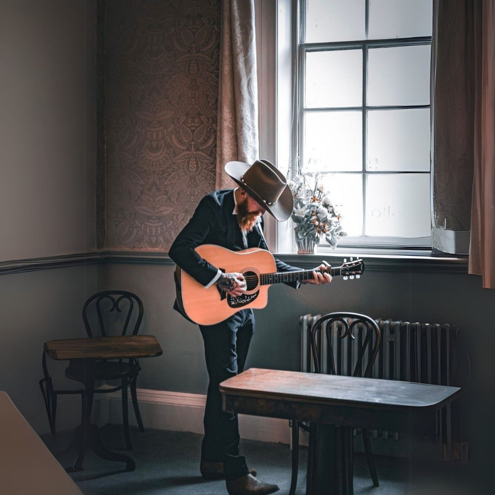 Country musician playing acoustic guitar by a window, creating a romantic and intimate wedding ceremony atmosphere.
