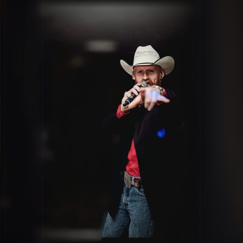 Adam Harding performing live on stage in a cowboy hat and red shirt, engaging the audience with an energetic performance. Professional country music entertainer.