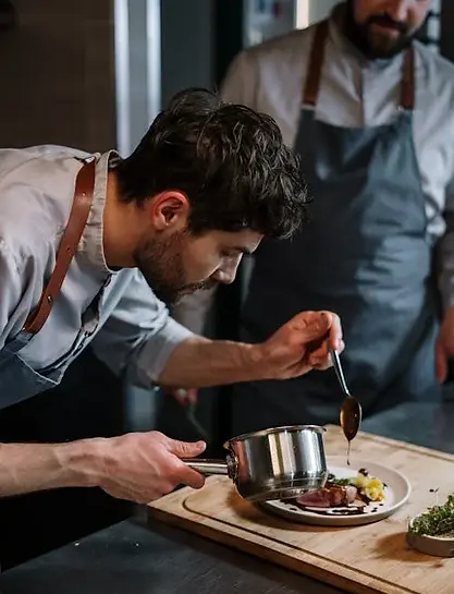 Man drizzles sauce on a dish while an instructor watches