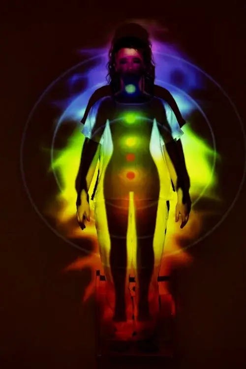 Full body picture of a person standing with arms to the side, with a projection of the 7 chakras projected onto their body.