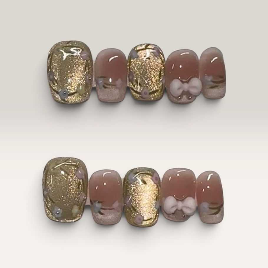 Gilded Blush press-on nails by M Press Beauty featuring soft blush pink, shimmering gold accents, delicate floral details, and 3D bow embellishments.