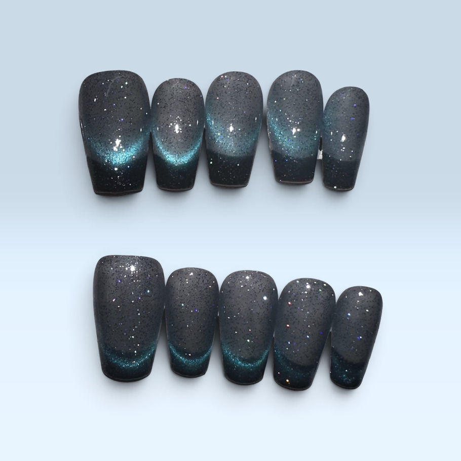 Midnight Aurora press-on nails featuring a smoky charcoal-black base, shimmering teal-blue magnetic cat-eye accents, and fine holographic glitter in a glossy short square shape.