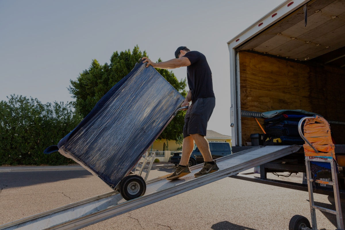 A man dollying a padded dresser up a box truck ramp