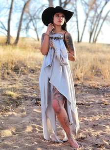 Woman wrapped in sheet in country field wearing cowgirl hat