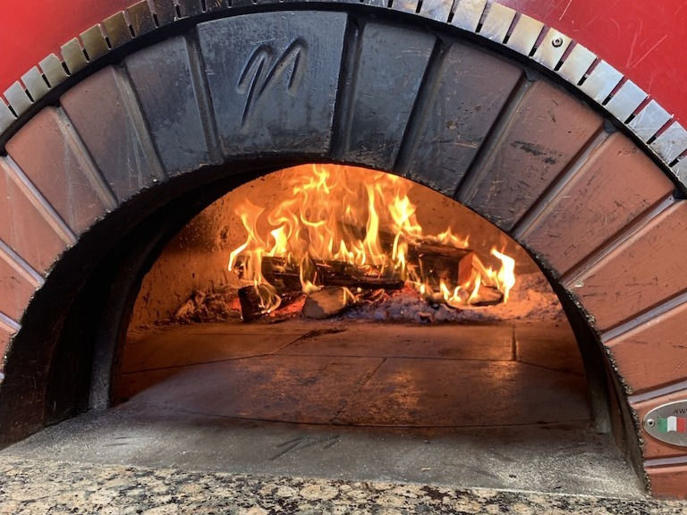 A photo of the mouth of Balsamo's Valoriani brick oven with the wood fire burning inside.