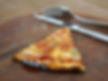 A close up of a single slice of reheated pizza with cutlery in the background.