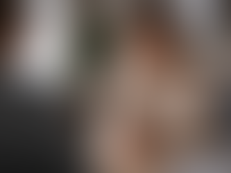 Eine junge Frau sitzt in einem Konfrontationsgespräch an einem Tisch. Ihre Körperhaltung wirkt angespannt, die Hände sind fest ineinander gelegt. Die zweite Person bleibt unscharf im Hintergrund, während die innere Anspannung der Frau deutlich sichtbar ist.