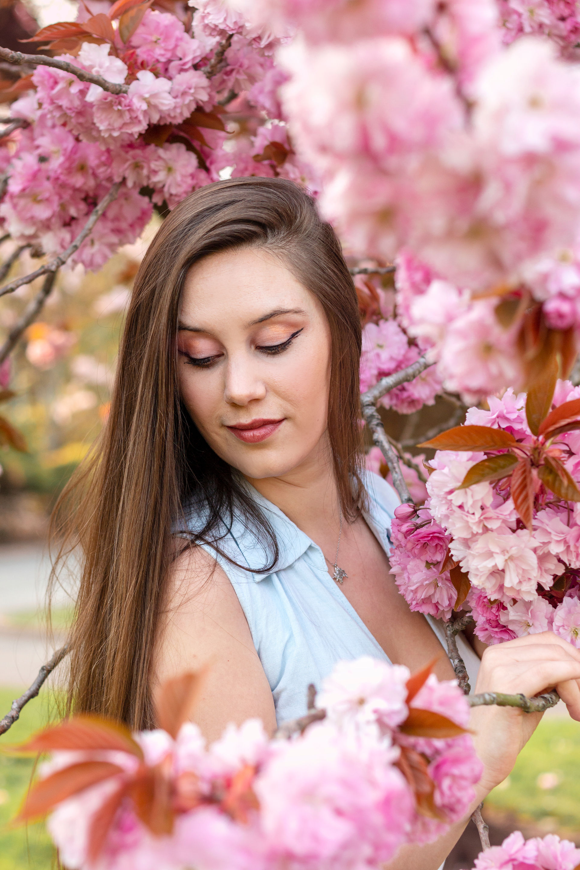 A young woman posing gracefully under a canopy of blooming flower trees in Alexandra Gardens, Cardiff, with soft pink and white blossoms framing her