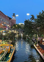 Night scene showing the bricktown canal with water taxi's, commercial red brick buildings on either side, with people enjoying the nightlife activities.