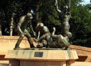 This large bronze sculpture is located on a round foundation about 3 feet high and 10 foot in diameter. There are four players in the very action-oriented sculpture. The tallest figure is a girl holding a bat up, obviously happy with the outcome of the play. Two figures are on the ground. Text on plaque:
"Play at Home"
Leonard McMurry Sculptor
Dedicated June 23, 1979
To all softball players and umpires worldwide.