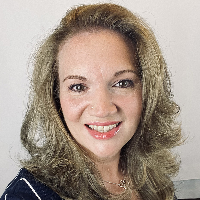 A headshot photo of a white woman with long, layered blonde hair. She is smiling at the viewer.