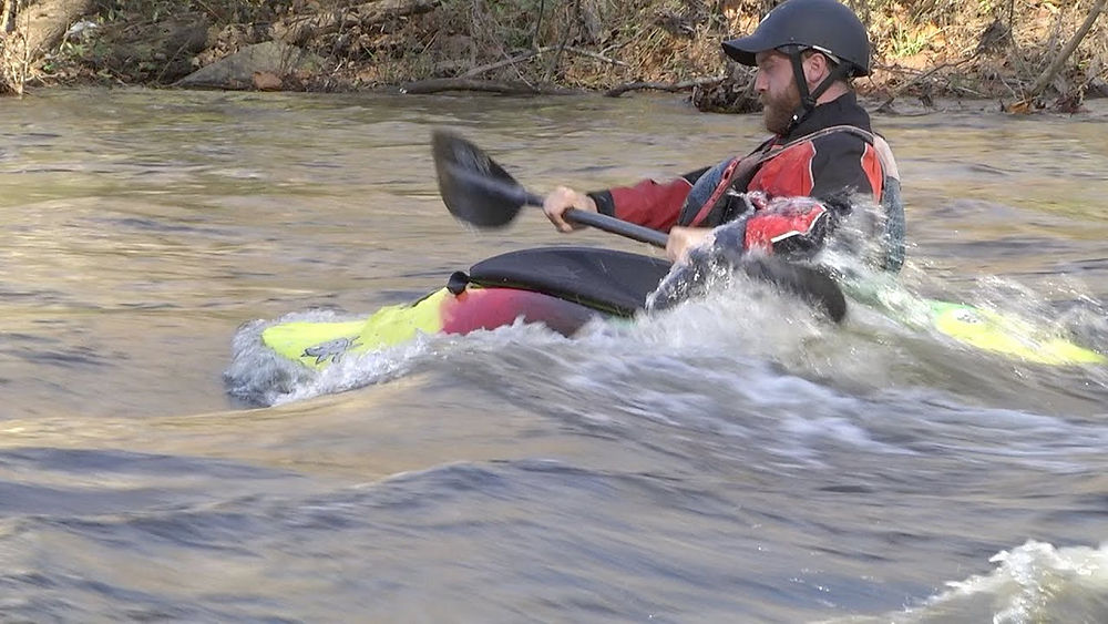 Kayaker in helmet paddling through rapids