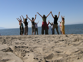 Frauenkreis am Strand mit offenen Armen zum Himmel gereckt