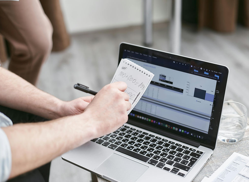 a man's arm writing figures in a notepad over a laptop