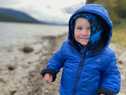 A Picture of K smiling and bundled in a snow suit next to a mountain lake