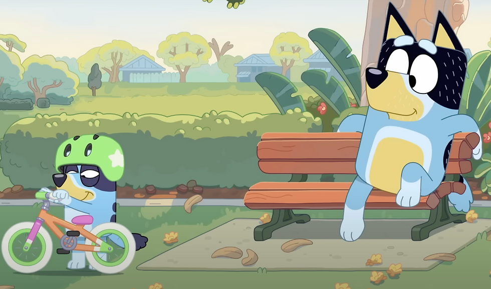 Bluey with a green bike helmet about to hop on her bike, while Bandit sits on a park bench watching.