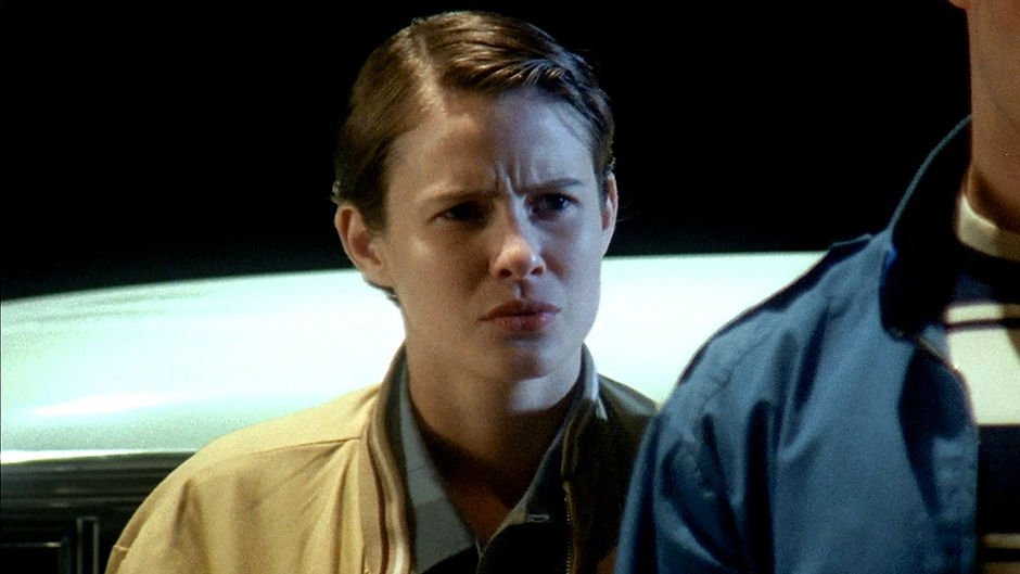 Sam, a transmasculine teenager played by American actress Linsey Godfrey, in the show Cold Case. He is standing outdoors at night, looking into the distance with a serious expression. He is light-skinned with short, dark brown hair, wearing a yellow coat over a green flannel shirt.