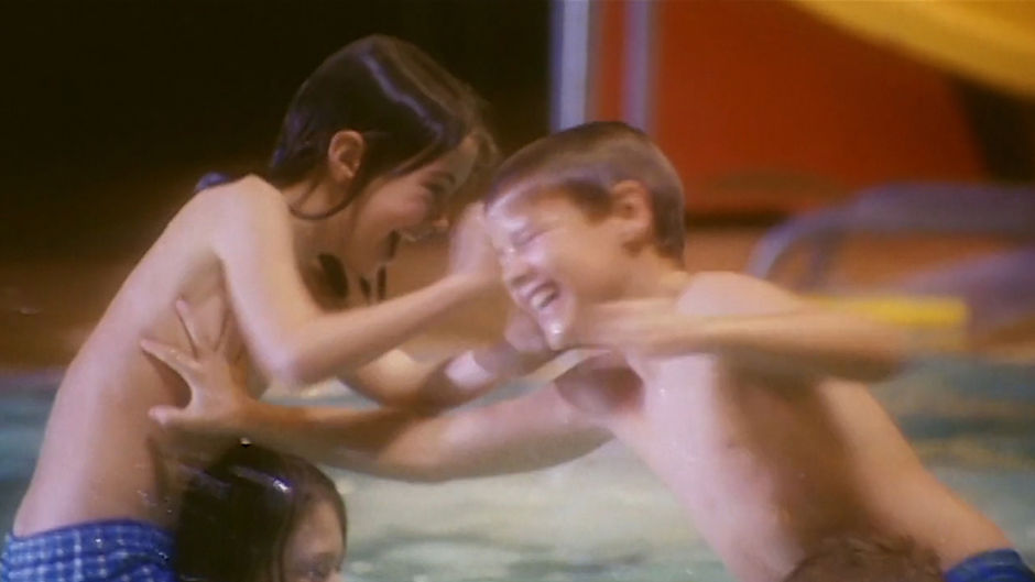 Robin, a trans child played by Canadian actress Matreya Fedor, in the film No Bikini. Robin is playing in a pool, splashing with another child, the pair laughing happily.