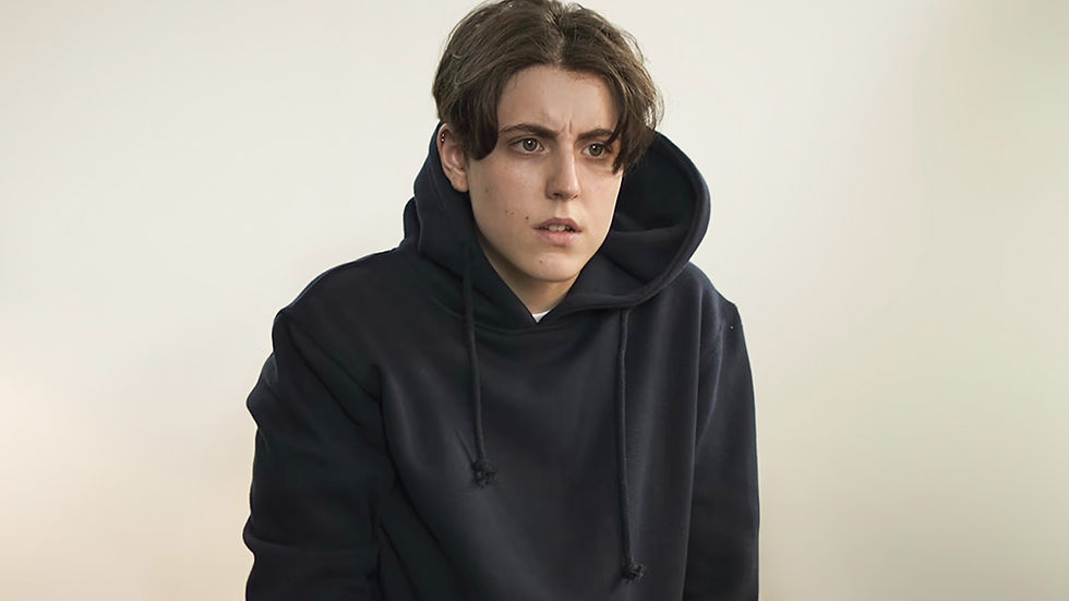 A trans man wearing a black hoodie. He has short dark hair.