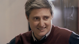 James, a trans man played by Australian gender non-conforming actor Del Herbert-Jane, in the film 52 Tuesdays. He is grinning, wearing a red sweater over a collared grey shirt. He has short, grey hair and is light-skinned.