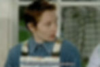 Lee, a trans man played by English actress Emma Lowndes, in the film Von Trapped. He is sitting next to his mother, talking to her. He is light-skinned with short, ginger hair, wearing a collared blue shirt. Captions in the image say, "I wanna have an operation."