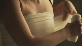 Emil, a teenage trans boy played by Danish actress Laura Emilie Hancock, in the short film BOY. He is a light-skinned young man standing indoors, wrapping bandages around his torso.