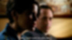 Sam, a transmasculine teenager played by American actress Linsey Godfrey, in the show Cold Case. He is sitting indoors and speaking, with captions in the image reading, "Why can't I just be who I am?" He is light-skinned with short, dark brown hair, wearing a blue flannel shirt. A light-skinned, older man is visible in the blurred background, looking at Sam with a neutral or concerned expression.