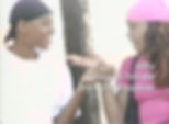 Tiffany, an Aggressive in the documentary The Aggressives, standing with his trans girlfriend, trans woman named Kelly. Tiffany is wearing a black head scarf and a white t-shirt. Kelly is wearing a pink headscarf and a pink t-shirt. The pair are gesturing at each other and smiling. Text in the image reads, "Kelly, male-to-female pre-op transsexual."