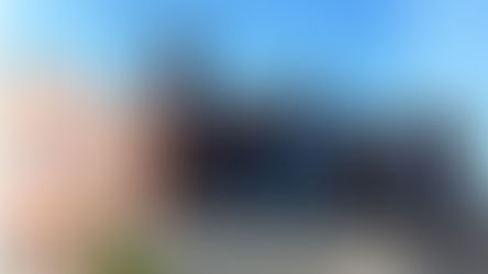 Red-brick building with large glass windows and tower against blue sky. Fenced yard in front, suggesting a secured area or campus.