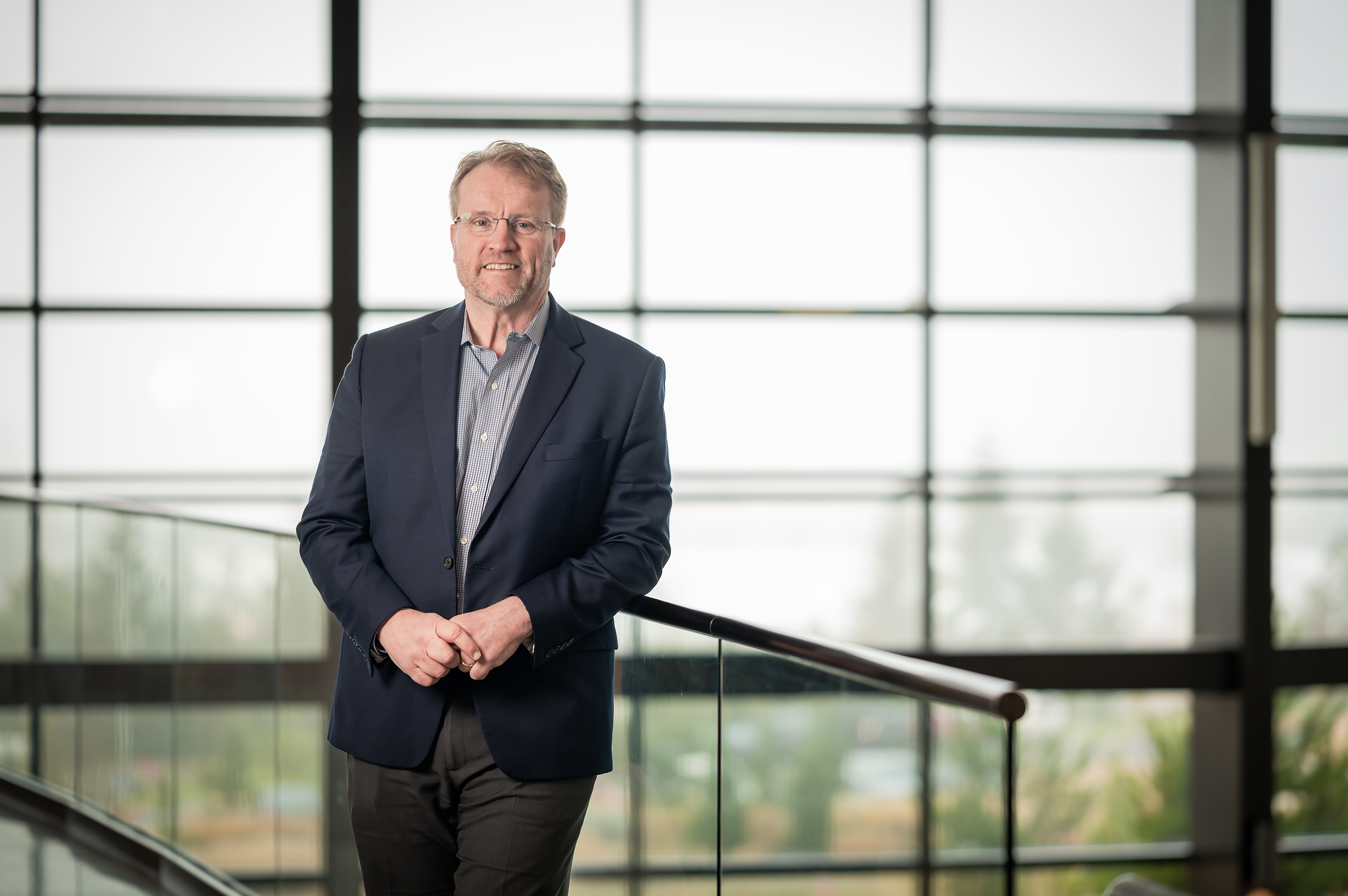 Man in a suit, standing near a railing, looking directly at the camera.