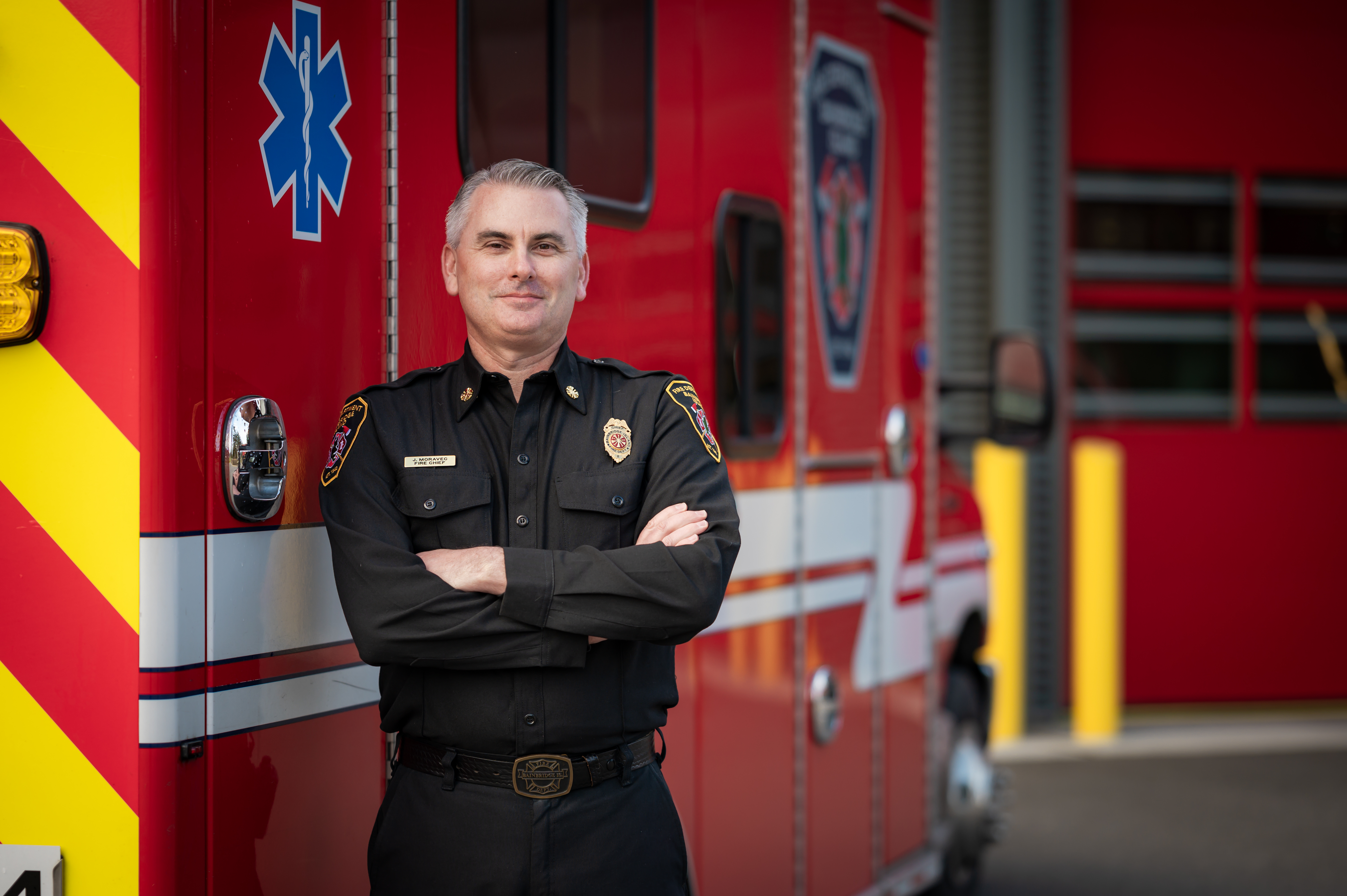 Man in uniform stands arms crossed by ambulance.