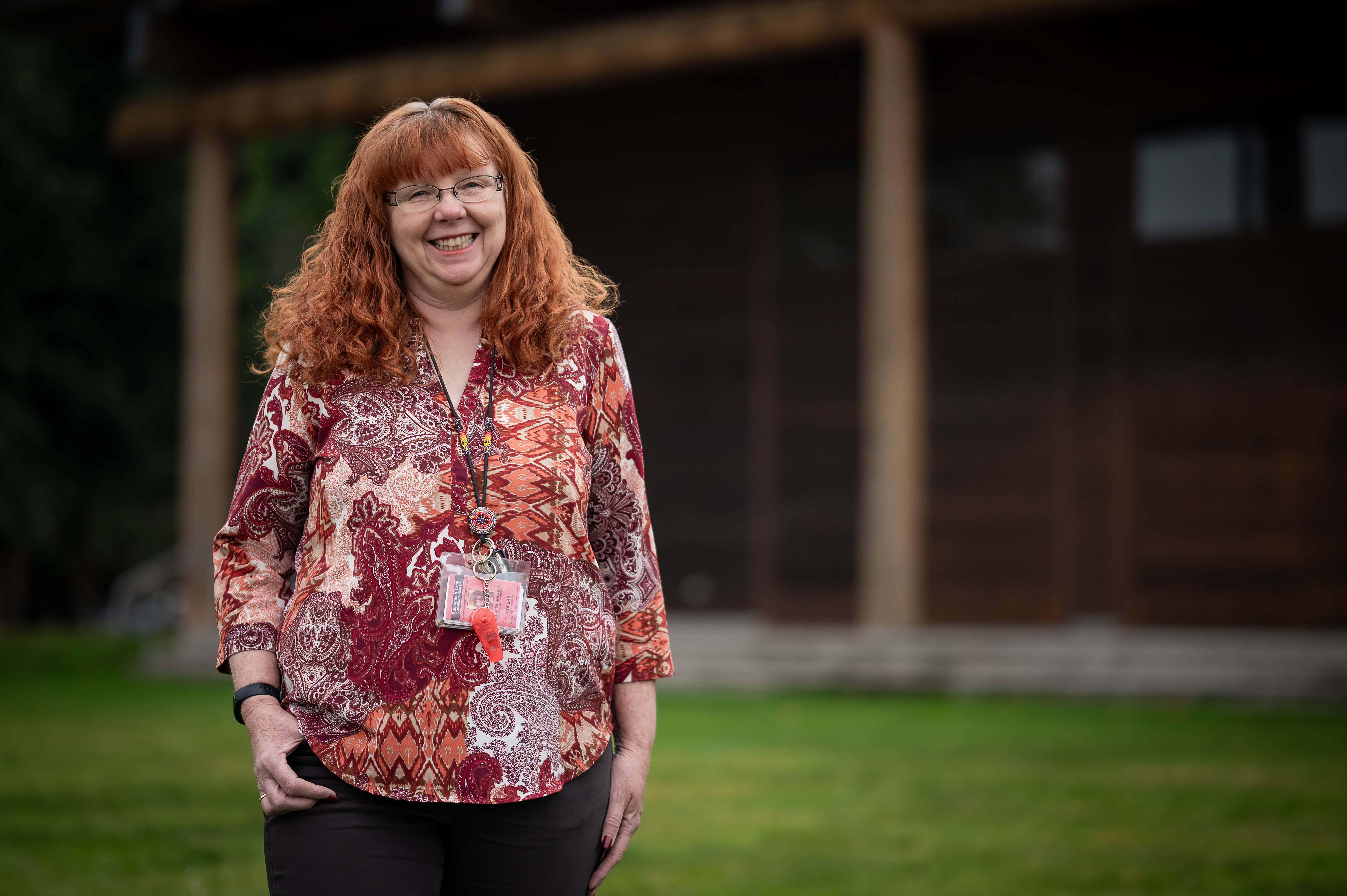 Woman with red hair smiles in front of a building on lawn.