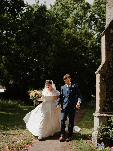 candid wedding photo of couple walking next to church