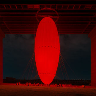 SpY’s OVOID (2024) is a site-specific installation composed of an illuminated egg-shaped structure suspended over a body of water, which challenges our perception of scale, space and movement. The newly commissioned artwork evokes the primordial form of the egg in its geometry, symbolizing the first place of refuge where life begins and maternal love manifests in its purest form.  Anchored to a bridge near Wadi Hanifah Dam, the 35-meter-high monumental ovoid looms above the lake. It emits a soft red glow from within, pulsing alternately to mirror the steady rhythm of life. From afar, the illuminated structure appears to multiply as it casts reflections on the water below.  This optical illusion invites the curious public to reflect on how our identity is always being shaped by the flow of life.