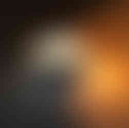The image shows a view through a large concrete or metal pipe at a desert landscape with a circular sculpture in the distance. The pipe's interior is textured and unevenly lit, with the right side catching the warm light of the setting sun, while the left is cooler. A series of dark, oval cutouts or marks are visible on the right side of the pipe's interior.  Through the opening of the pipe, the landscape of the desert extends and reveals another, smaller circular sculpture standing upright on the horizon line. The sky is a soft gradation of color, indicating either sunrise or sunset, with light clouds adding depth and texture. The overall mood of the scene is tranquil and serene, with the framing of the pipe creating a sense of perspective and focus in the vast, open space.