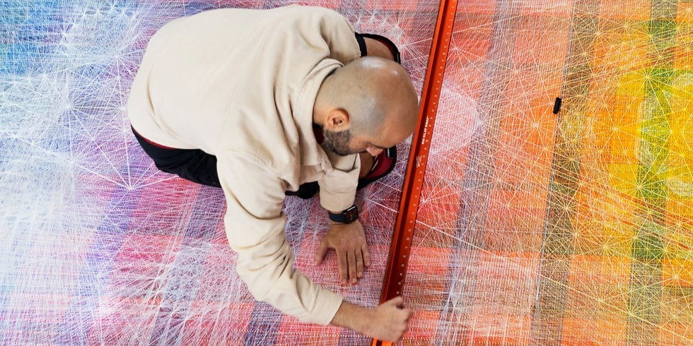 Nima Nabavi kneeling, drawing with a red ruler on a colorful geometric floor. Background shows intricate patterns in blue, red, and yellow shades.