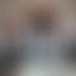 An image showcasing the interior of the entrance to a building. The door itself is a black-framed glass door, above which is a stained-glass window composed of many squares, each filled with a different vivid color and a unique design or image, adding an artistic flair to the entrance. The walls flanking the entrance are white at the top and feature a tiled section below, using black and white tiles. A gray ribbed mat lays just inside the door on the floor tile. On the left, a red fire hose cabinet is mounted to the wall. Outside, the sidewalk and street can be seen through the glass door, along with buildings across the street.