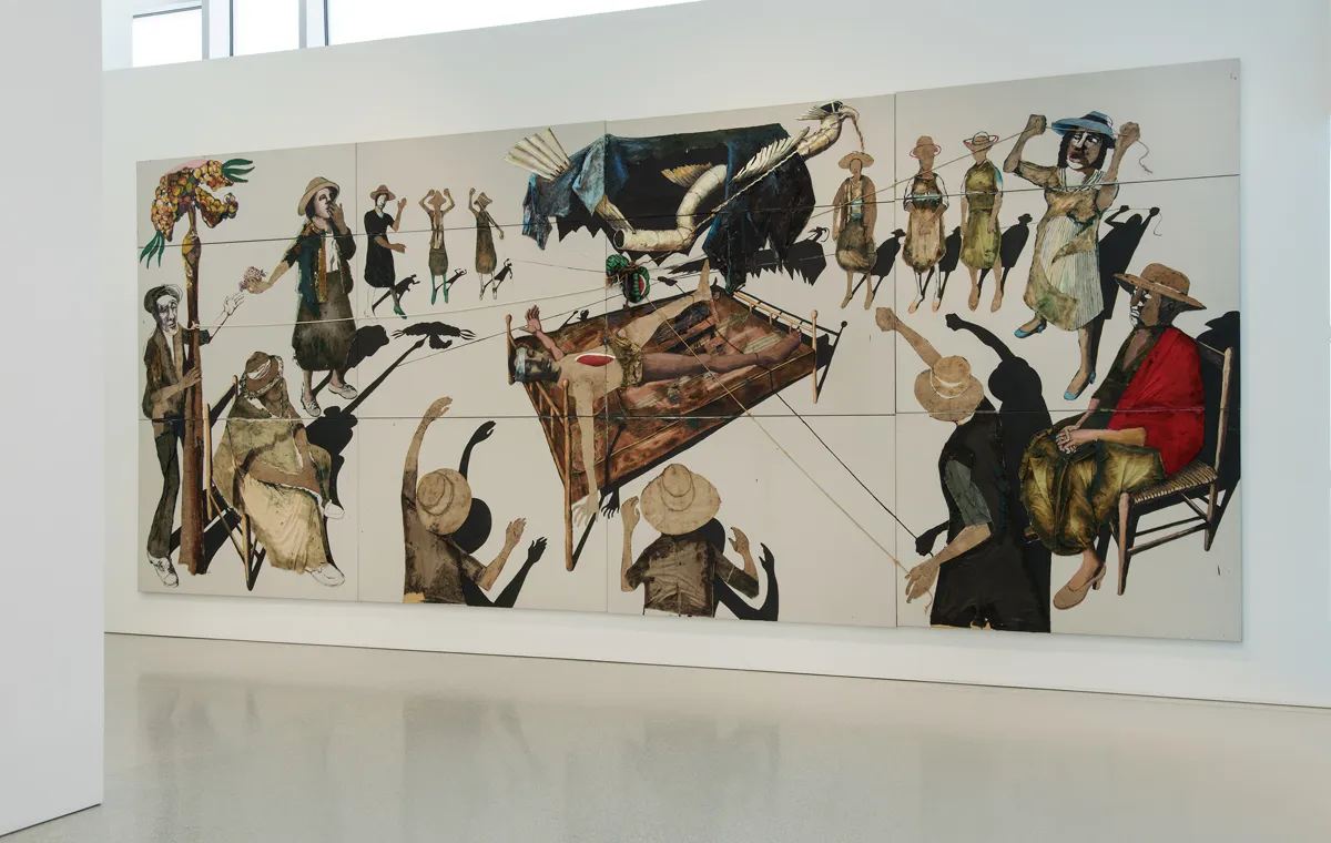 The artwork consists of numerous square tiles assembled together to create a continuous mural or tableau. The mural is mounted on a gallery or museum wall, with a portion of the wall visible at the bottom of the frame.  The artwork features an array of figures rendered in a rustic, folk-art style, some depicted as silhouettes and others with varying degrees of detail and color. The figures appear to be participating in or observing a scene of symbolic or ritualistic nature.  In the center of the artwork, a bed or platform is suspended at an angle, upon which lies a figure. This central figure has a visible area of red, possibly an injury or symbolic marking. A large, dark shape resembling a bird or shrouded figure looms over the bed.  The figures around the bed are depicted in various poses, some with arms raised, possibly pulling on strings or ropes that seem to be connected to the bed. These figures wear a mix of clothing styles, with some donning hats.  The color palette is muted, with earth tones and blacks predominating, although there are splashes of color in the clothing and details of the figures. The tile medium gives the artwork a textured, segmented appearance.