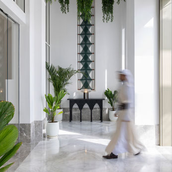 exemplar art work from artelier's art collection at raffles al areen palace, bahrain, featuring a bahraini man walking in a blurred motion in front of a woven green wall piece tapestry