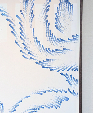 A high-angle close-up showcases an abstract pattern on a white background. The pattern is characterized by chains of small, blue oval shapes arranged in curved, flowing lines. These lines seem to emanate from the lower left corner of the frame, arching and swirling upwards and towards the right. The density of the blue shapes varies, creating a sense of movement and depth. The contrast between the cool blue and the stark white background emphasizes the organic and dynamic nature of the pattern. The overall aesthetic is clean, minimalist, and visually engaging.