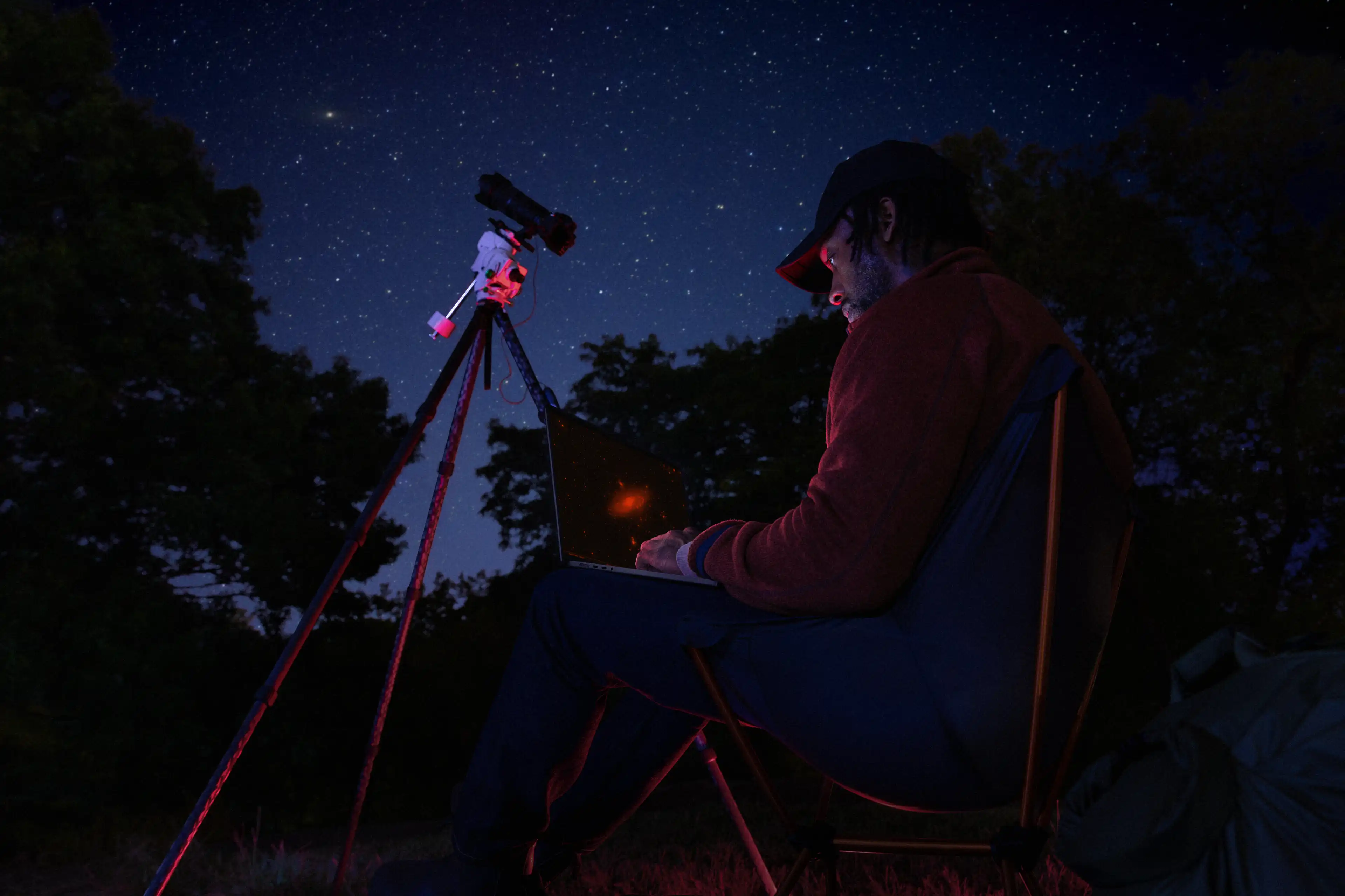L’utilisateur d’un MacBook Pro est assis dehors à coté d’un téléscope sous un ciel étoilé.