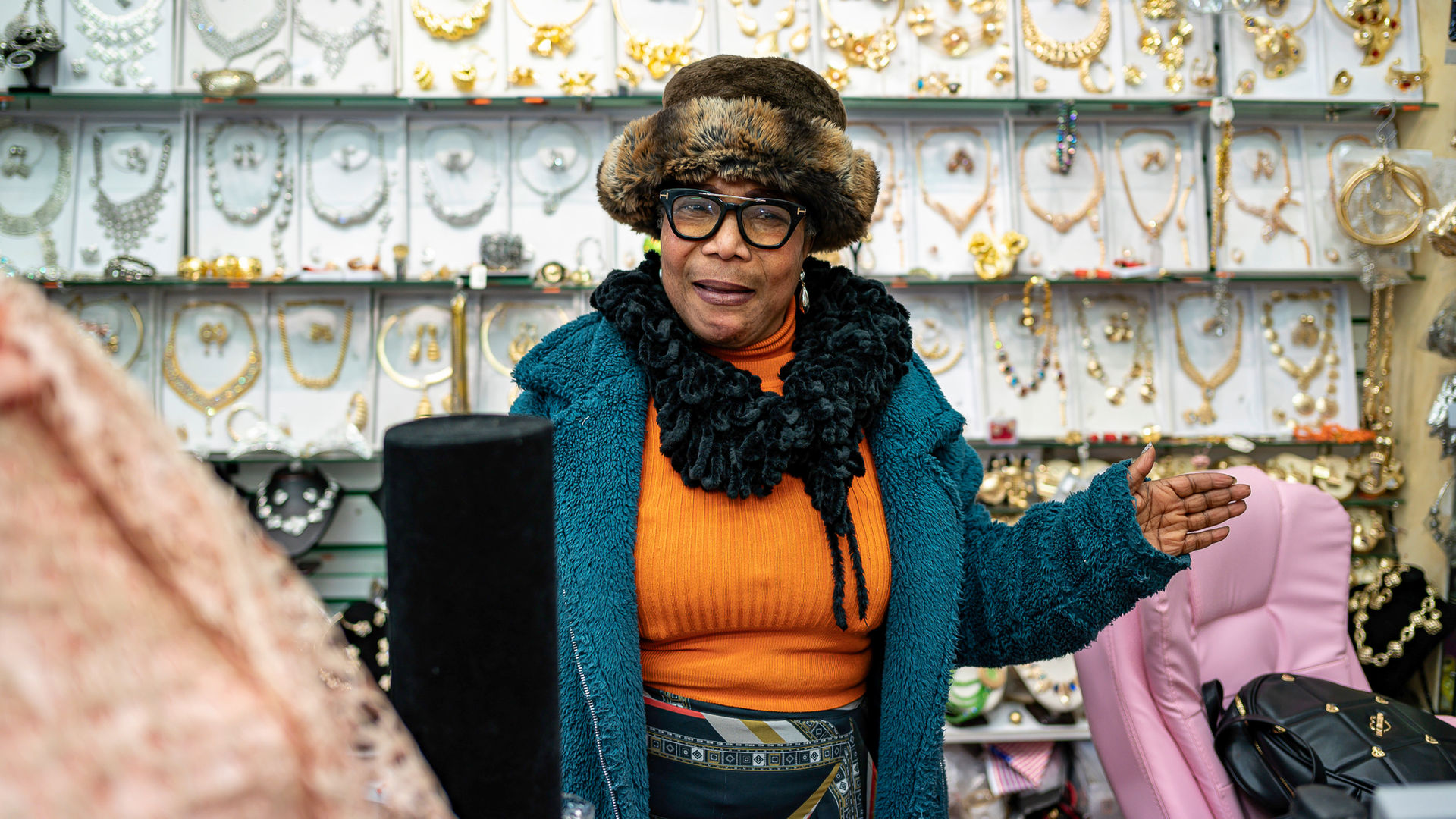Woman wearing glasses and hat gestures towards jewelry at East Street Market