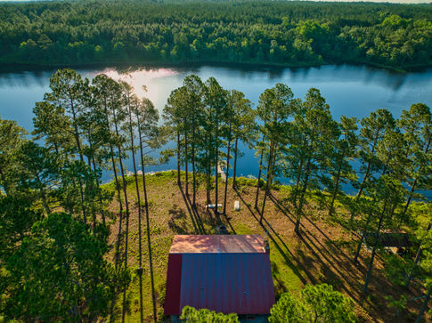 Aerial drone photograph of a cabin on a wooded lakefront lot.