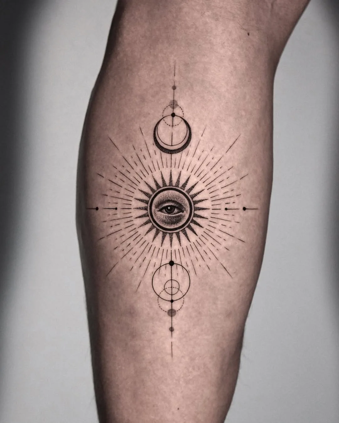 Black and grey fineline tattoo on the shin featuring a radiating sun with an eye at its center, a crescent moon above, and geometric circles below, all connected by fine linework. By Kiljun at Seoul Ink Tattoo, Gangnam, Seoul, South Korea.